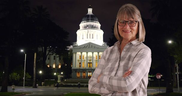 Old female person looking content crossing arms outside at night in Sacramento - Photo, Image