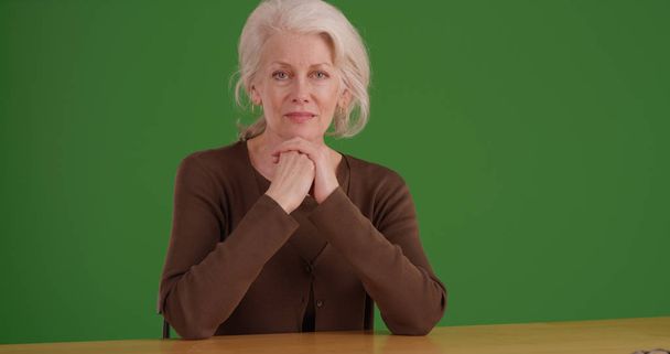 Lovely кавказьких старенька сидячи за столом, дивлячись на зелений екран камери - Фото, зображення