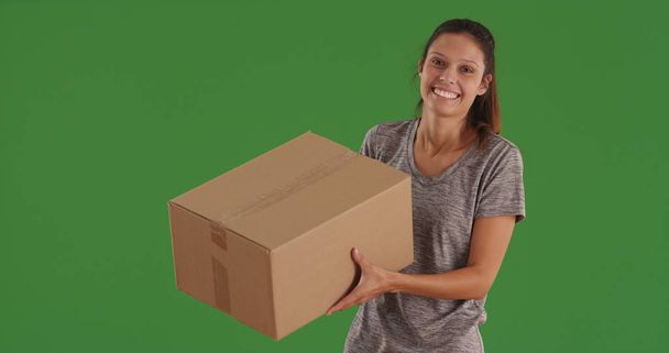 Joyful wit meisje uitvoering van grote kartonnen doos staande op groen scherm - Foto, afbeelding