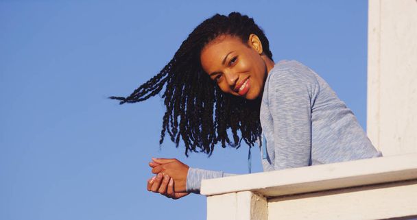 Onnellinen musta nainen nojaa kiskoon hymyillen
 - Valokuva, kuva