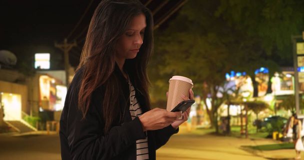 Millennial woman reading text from friend while on Costa Rican street at night - Photo, Image