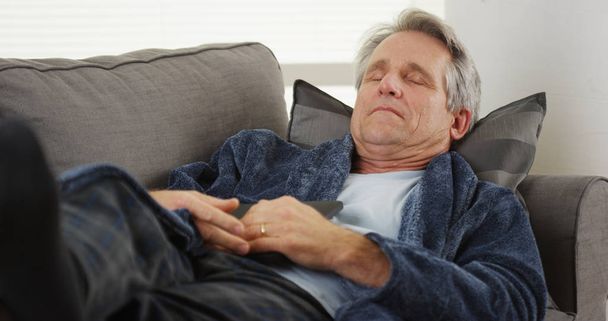 Зрелый мужчина спит на диване, держа планшет
 - Фото, изображение
