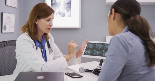 Young latina patient reviewing ct scan of cranium with middle aged doctor - Photo, Image