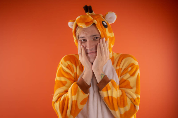 pajamas in the form of a giraffe. emotional portrait of a guy on an orange background. crazy and funny man in a suit. animator for children's parties - Foto, Imagen
