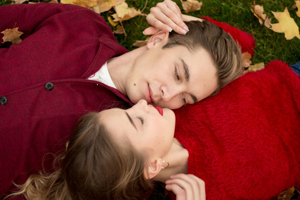 Close-up of a girl and a guy in red sweaters, heads, lips nearby, love and attraction in a pair. second to kiss.love on a date. couple lies on yellow leaves - Photo, Image