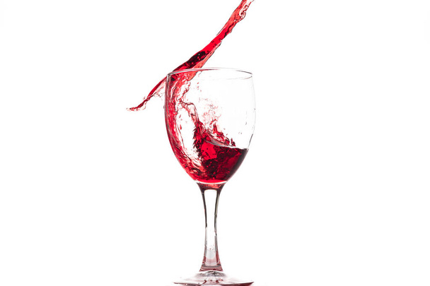 Rode wijn in een glas valt en wordt gemaakt van splash en spatten op een witte achtergrond. - Foto, afbeelding