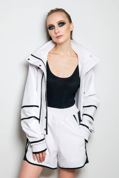 Portrait of fashion model in white sports suit. Girl in unzipped jacket, sleeveless t-shirt and wide shorts - sportive outfit. - Foto, afbeelding