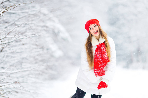 beautiful girl look into the distance and shows grimaces in white-red winter clothes on the background of the park covered with snow - Zdjęcie, obraz
