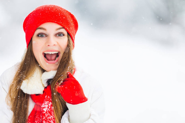 girl in red hat and scarf on which there is snow looks in the camera lens and opened her mouth - Photo, Image