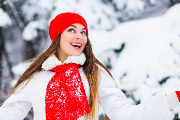 niña en ropa de invierno mira hacia arriba y sonríe contra el fondo de los árboles cubiertos de nieve
 - Foto, Imagen