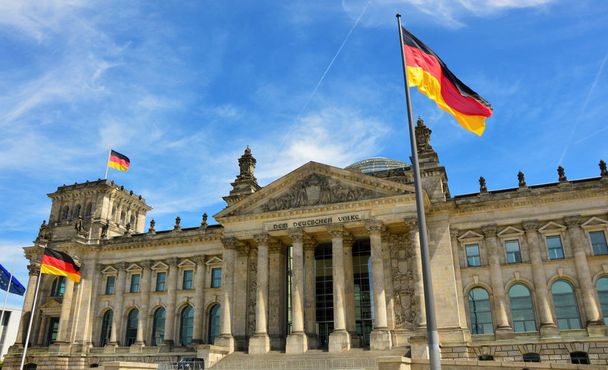 Bandiere tedesche sventolano nel famoso edificio del Reichstag, sede del Parlamento tedesco (Deutscher Bundestag), in una giornata di sole con cielo azzurro e nuvole, quartiere Mitte di Berlino centrale, Germania - Foto, immagini