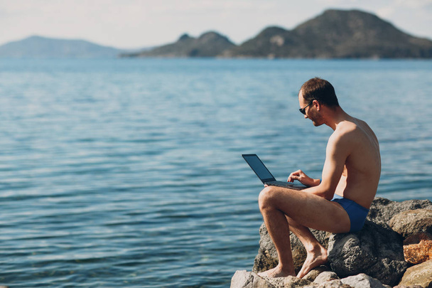 Молодий чоловік фрілансер працює з ноутбуком біля моря
 - Фото, зображення