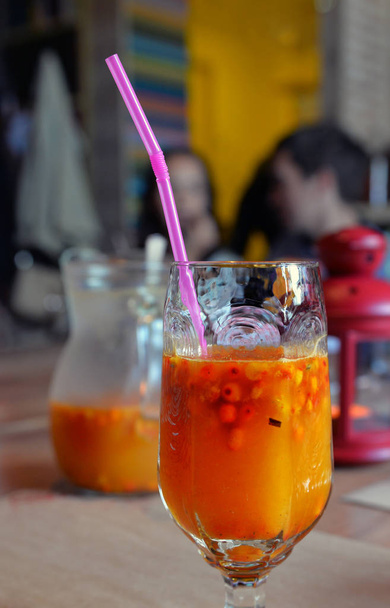 Jus d'argousier orange vif en verre avec tube à boire dans un caf confortable
 - Photo, image
