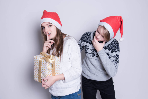 shh! Geheimhaltung. Porträt von drei glücklichen Teenagern mit Weihnachtsmannmütze und weißen warmen Pullovern. Frohe Weihnachten und frohe Feiertage. Familienurlaub, Party vor weißem Hintergrund. Weihnachten. - Foto, Bild