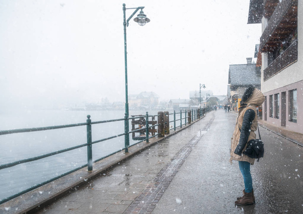 Γυναίκα να στέκεται στο δρόμο, βλέπουν τις νιφάδες χιονιού, Χάλστατ, Αυστρία, μια χιονισμένη μέρα του χειμώνα. - Φωτογραφία, εικόνα