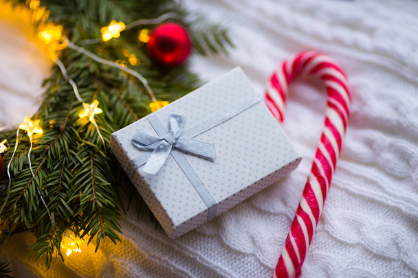 Coffret cadeau blanc et canne caramel près de couronne de sapin avec boules de Noël rouges et enroulé avec guirlande lumineuse avec lumière chaude sur plaid tricoté blanc. Décoration de la maison Nouvel An
 - Photo, image