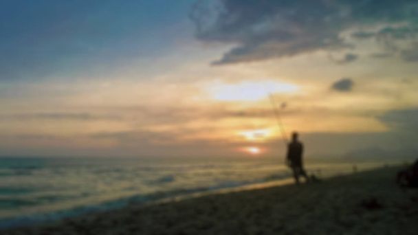 ein schöner verschwommener Hintergrund mit der Silhouette eines Mannes beim Angeln an einem Strand in der Nähe des Sonnenuntergangs - Foto, Bild