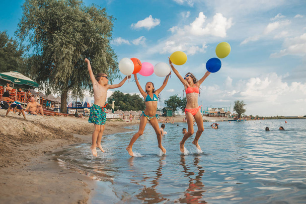 Niños felices jugando con globos en el mar. Niños divirtiéndose al aire libre. Vacaciones de verano y concepto de estilo de vida saludable
 - Foto, imagen