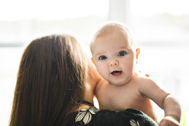 A Portrait of happy baby with cheerful mother at home window - Foto, Bild