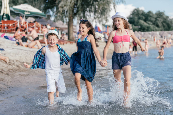 Denizde oynayan mutlu çocuklar. Çocuklar dışarıda eğleniyor. Yaz tatili ve sağlıklı yaşam tarzı konsepti - Fotoğraf, Görsel