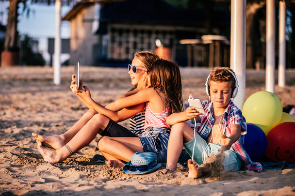 Olumlu çocuklar cep telefonları ile oynarken portresi ve kumsalda birlikte tablet - Fotoğraf, Görsel