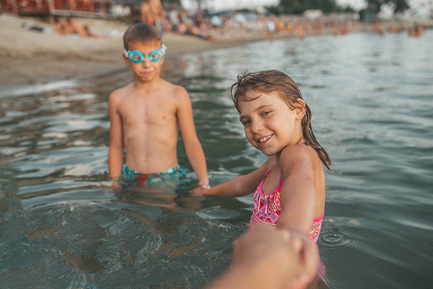 Mutlu çocuklar denizde oyun. Çocuklar tutan eller ve onlarla gitmek annelerini davet ediyoruz. Yaz tatili ve sağlıklı yaşam konsepti - Fotoğraf, Görsel
