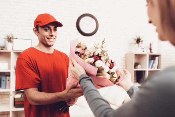 Flowers Delivery. Flowers Deliveryman. Man with Box is Funny Accessory. White Interior. Deliveryman Arab Nationality. Courier in Orange Clothes. Express Delivery. Gives Flowers Girl. Pink Package. - Foto, immagini