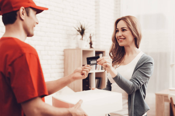 Courier Delivery. Woman Gives Bank Card. Worker Man Arab Nationality. White Interior. Deliveryman Arab Nationality. Courier in Orange Clothes. Express Delivery. Gives Package. Pays Delivery Bank Card. - Foto, imagen