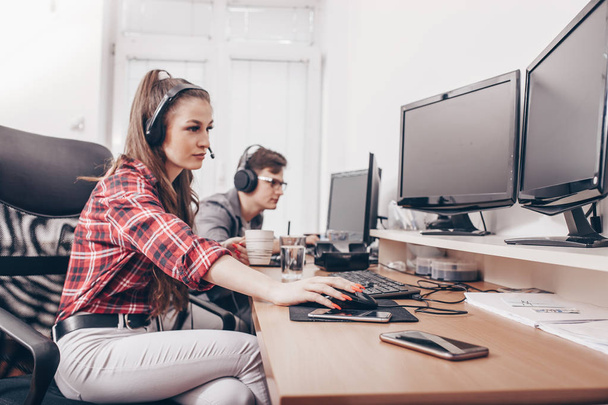 Portret van jonge lachende vrouw met hoofdtelefoon werken met mannelijke collega bij computer balie in kantoor - Foto, afbeelding
