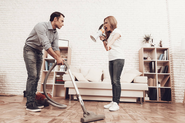 Man and Woman in Apartment. Man Cleans Room. Man with Vacuum Cleaner. Male Washes Brown Floor. Woman with Megaphone Shouts Scared Man. Woman Control Cleaning Rrocess. Cleaning Process. - Фото, изображение
