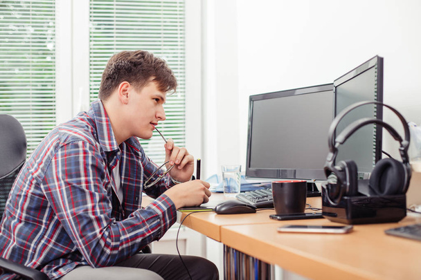 若い男が、オフィスでは、カジュアルな服装でグラフィック デザイナー デスク デスクトップ コンピューター上で動作するグラフィック タブレットを使用してのショット. - 写真・画像