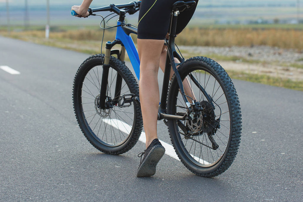 Κορίτσι σε ένα ποδήλατο βουνού σε offroad, όμορφο πορτρέτο ενός ποδηλάτη στο ηλιοβασίλεμα, Fitness κορίτσι βόλτες ποδήλατο βουνού σύγχρονη ινών άνθρακα. - Φωτογραφία, εικόνα