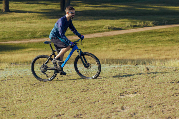 Ciclista en pantalones cortos y jersey en una moderna bicicleta rígida de carbono con horquilla de suspensión neumática
 - Foto, Imagen