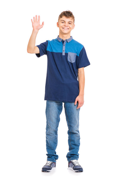 Full length portrait of young caucasian teen boy isolated on white background. Funny teenager stretching his right hand up for greeting. Handsome child waving hand, looking at camera and smiling. - Photo, image
