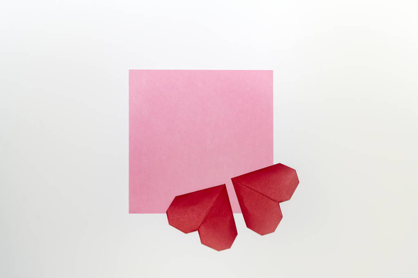 Skład z papieru origami serca na różowy kawałek papieru na białym tle z miejsca kopii. - Zdjęcie, obraz
