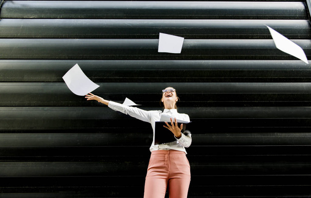 Портрет молодой предпринимательницы в деловой одежде, выбрасывающей бумажные документы на улицу
 - Фото, изображение