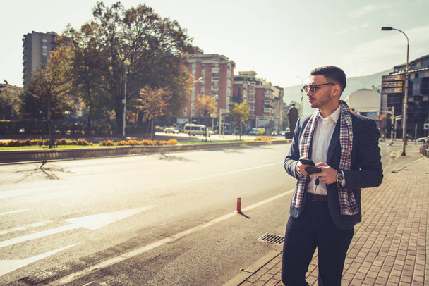 Молодий сучасний бізнесмен знаходиться на вулиці, вигулюючи центр міста і дивлячись зацікавлені в пробці
 - Фото, зображення