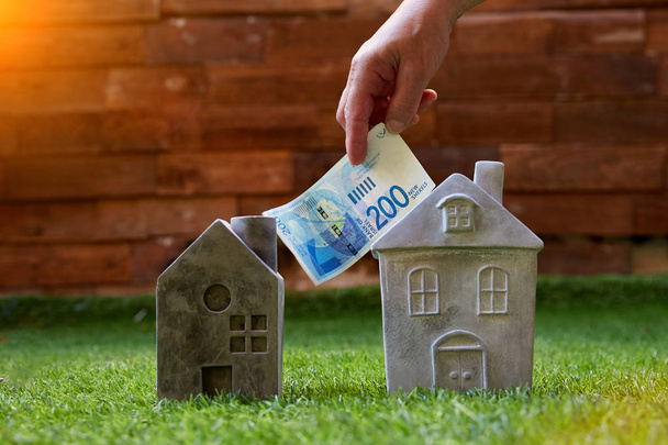 Crop man investing Israeli new shenkel into mortgage putting bill on grass with stone houses in sunlight - Φωτογραφία, εικόνα