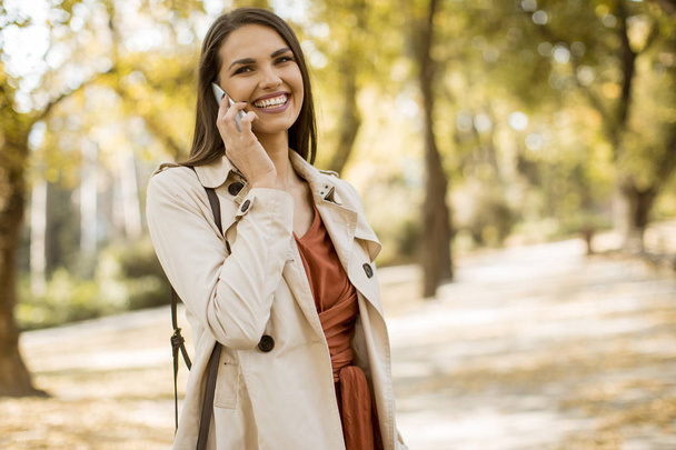 Onnellinen nuori nainen käyttää matkapuhelinta syksyllä puistossa kauniina päivänä
 - Valokuva, kuva