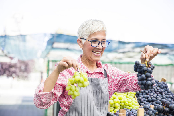 Portret senior kobiety sprzedaje winogron na rynku - Zdjęcie, obraz