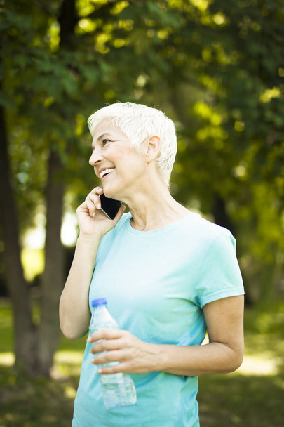 Portrait of sporty senior woman using mobile phone in the park - Foto, imagen