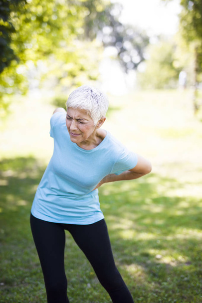 Mujer mayor de fitness frotando los músculos de la parte baja de la espalda. Dolor de espalda
 - Foto, imagen