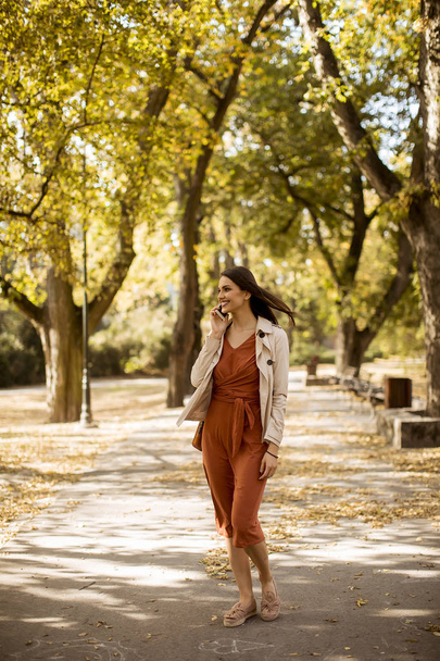 Happy young woman using cell phone in autumn park on beautiful day - Foto, imagen
