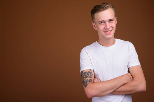 Young handsome man with blond hair smiling against brown background - Fotografie, Obrázek