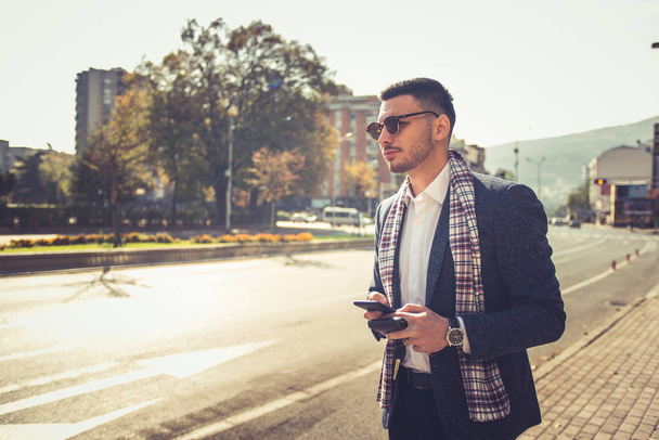 Молодий бізнесмен у костюмі з шарфом виглядає сучасно під час прогулянки в центрі міста
 - Фото, зображення