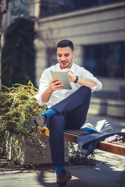 Empresário urbano está sentado no banco no centro da cidade, olhando para seu tablet e desfrutando do bom tempo
 - Foto, Imagem