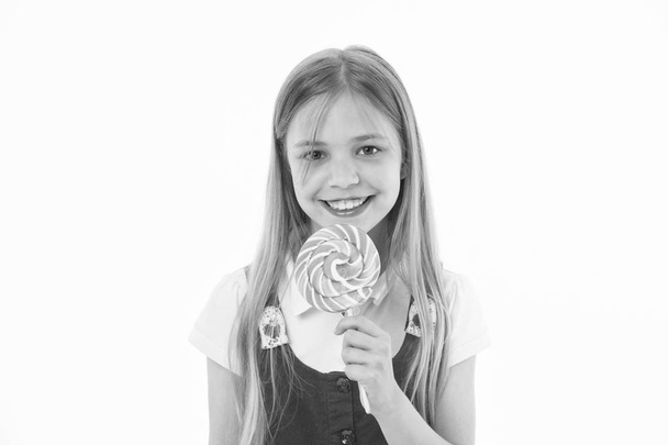 Girl eating big candy on stick or lollipop. Sweet tooth concept. Girl on smiling face holds giant colorful lollipop in hand, isolated on white background. Kid with long hair likes sweets and treats - Photo, Image