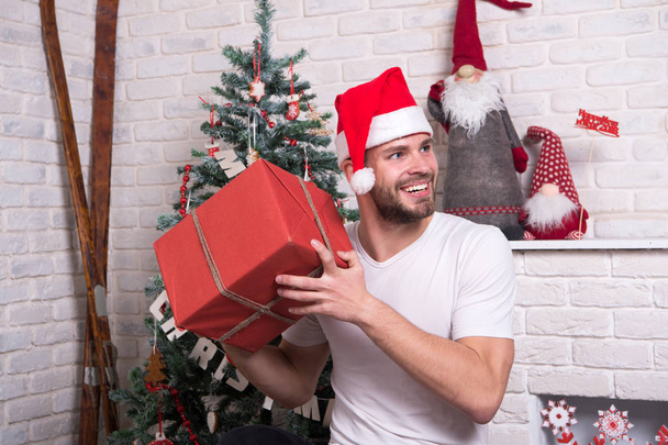 man in santa hat hold christmas present. online christmas shopping. New year scene with tree and gifts. delivery christmas gifts. The morning before Xmas. happy santa man. Office christmas party - Foto, afbeelding