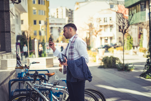 Un homme d'affaires urbain est dehors sur la place de la ville, debout à côté de son vélo et prenant des photos dans le miroir des bâtiments
 - Photo, image