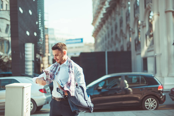 Hombre de negocios guapo está sosteniendo su cuaderno y café mientras camina por la calle disfrutando del clima ventoso
 - Foto, imagen